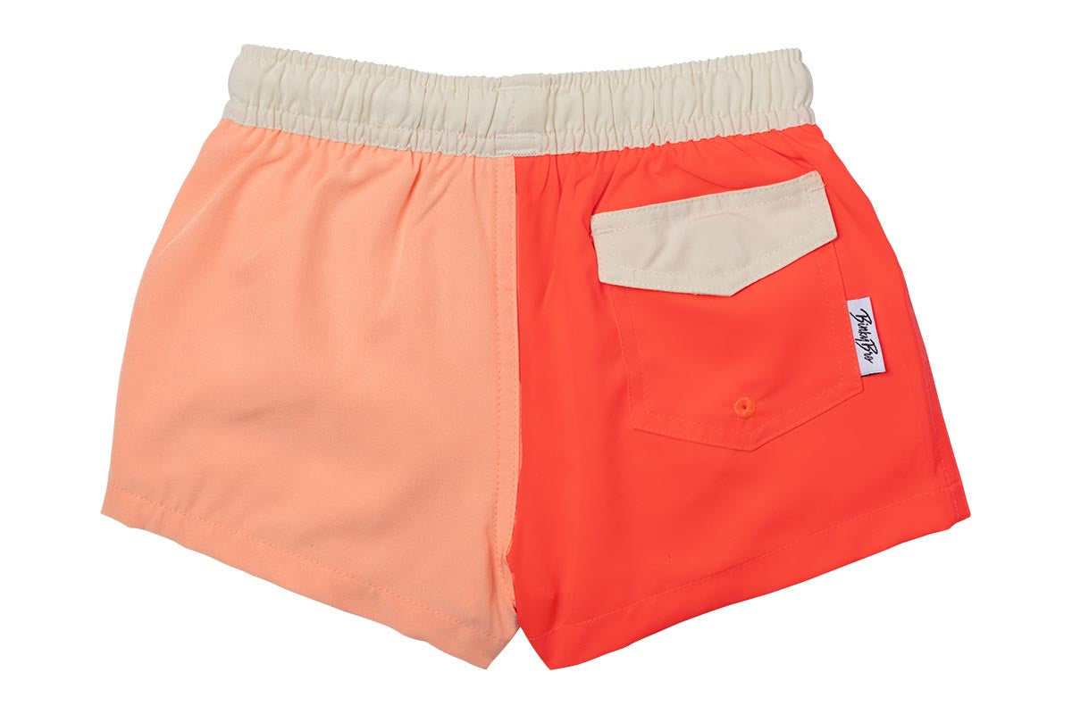 Stylish two-tone swim shorts for kids featuring a peach and coral color scheme with a back pocket. Perfect for beach days.
