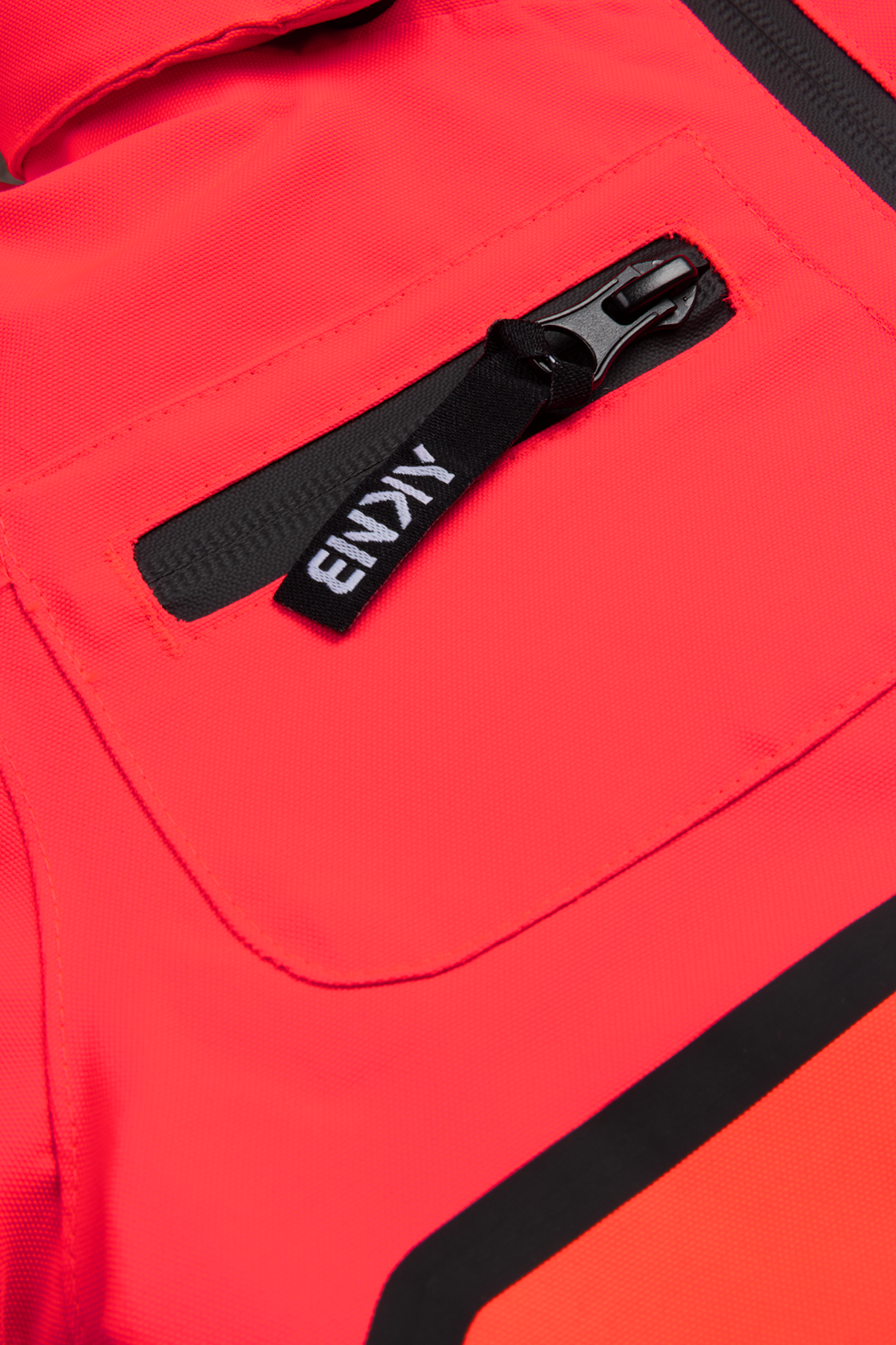 Close-up of a vibrant red jacket featuring a zippered pocket with a black pull tab, showcasing a stylish and functional design.