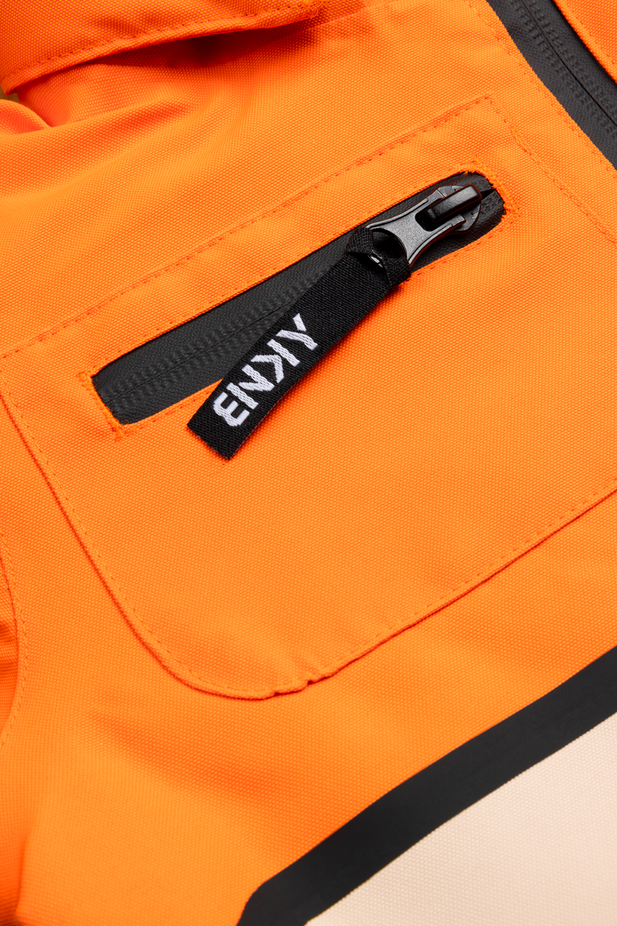 Close-up of the 99-90 BNKY Dragonfire jacket featuring an orange fabric with a zippered pocket and branded tag.