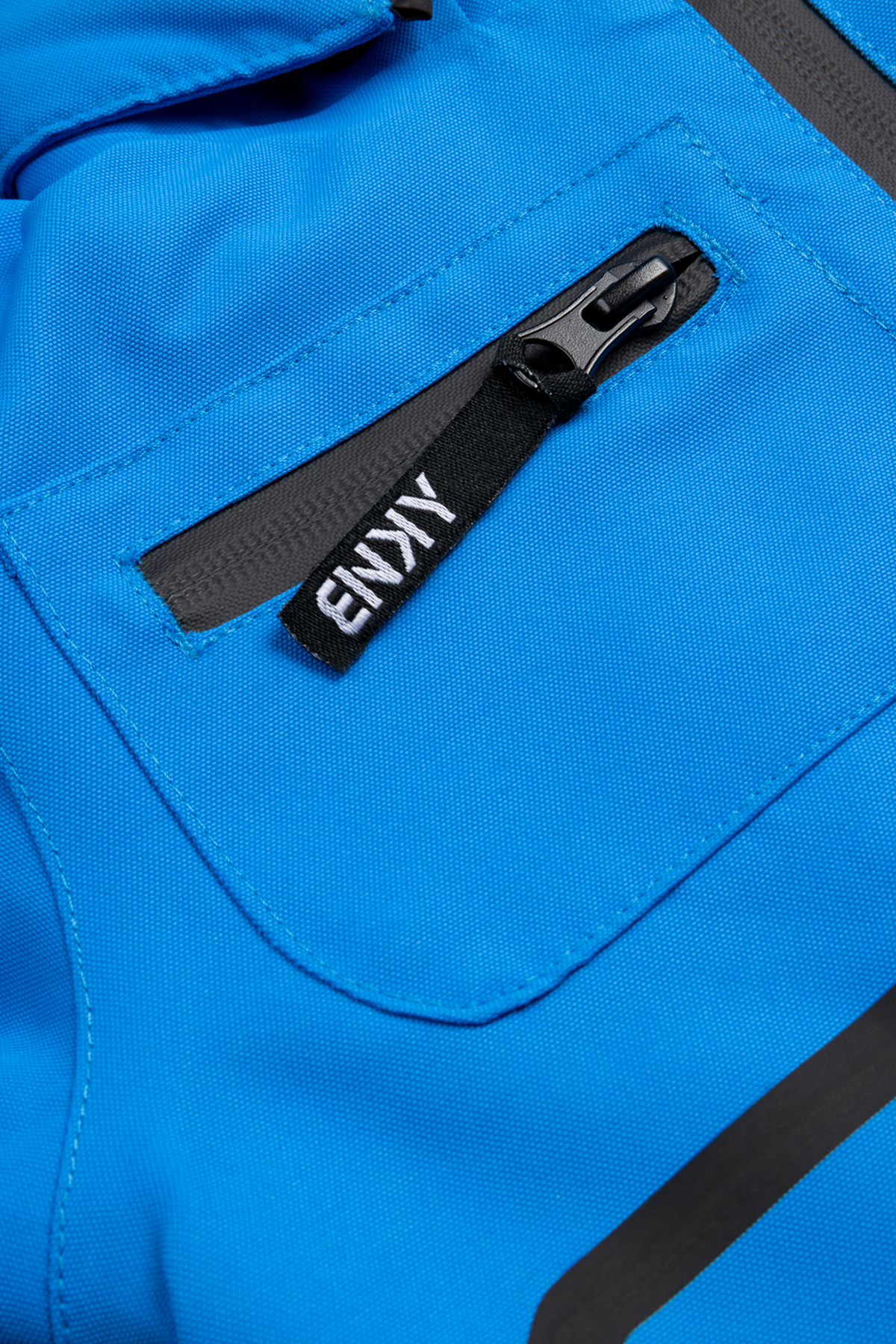 Close-up of a cobalt blue fabric featuring a zippered pocket with a black tag labeled "BNKY," showcasing stylish design details.