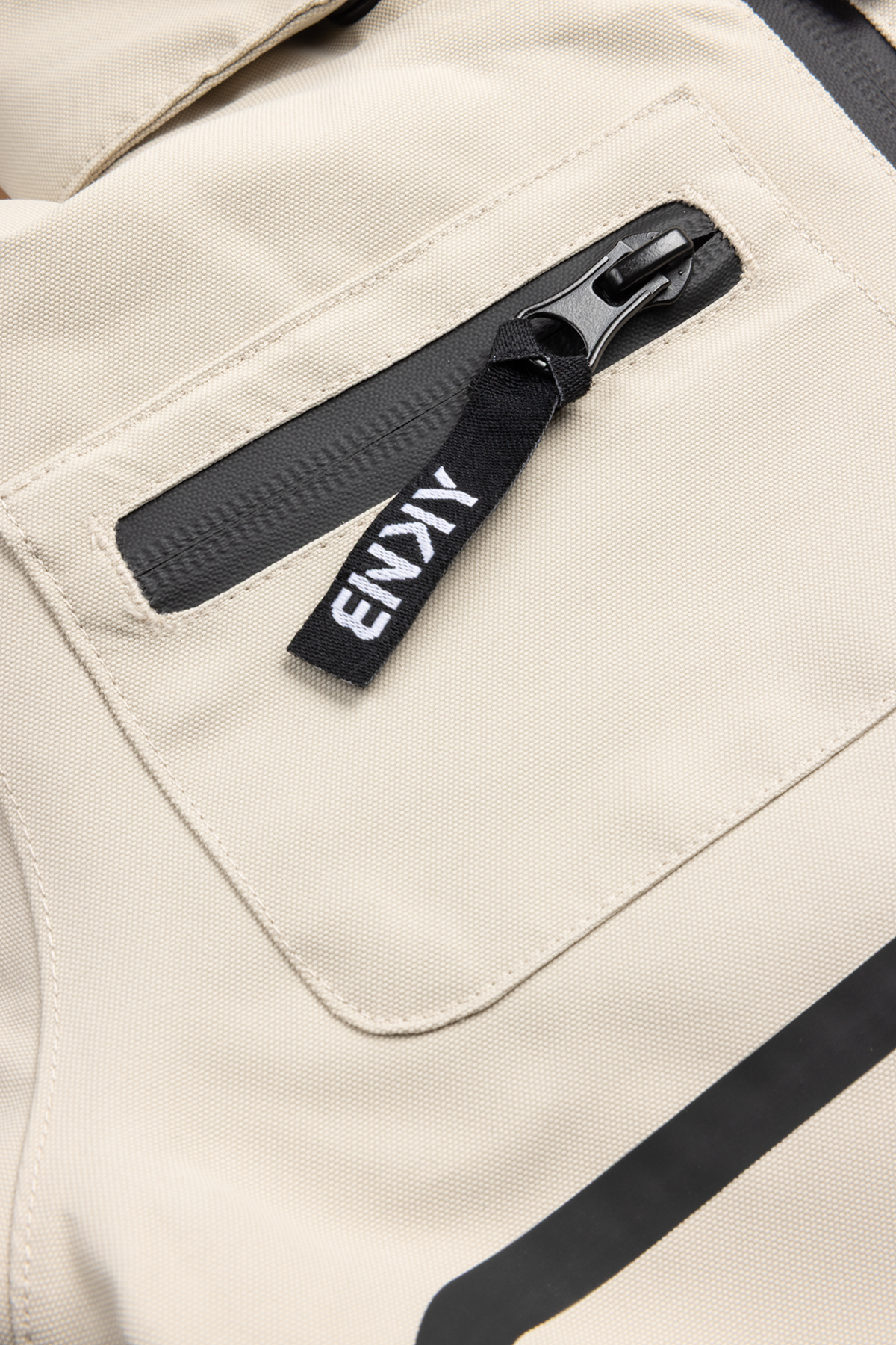 Close-up of a beige fabric with a zippered pocket featuring a black pull tab labeled BNKY, showcasing stylish design details.