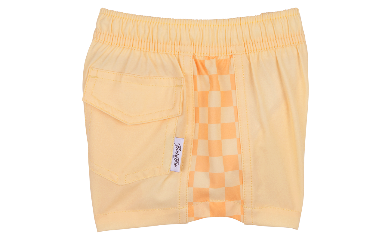 Peach checkered swim shorts with an elastic waistband and a side pocket, designed for infants and toddlers.