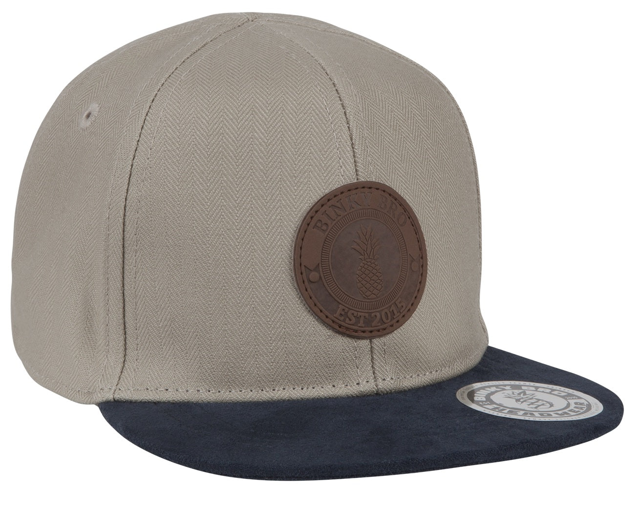 Stylish beige snapback hat with a navy brim and a textured leather patch featuring a pineapple logo. Perfect for kids.