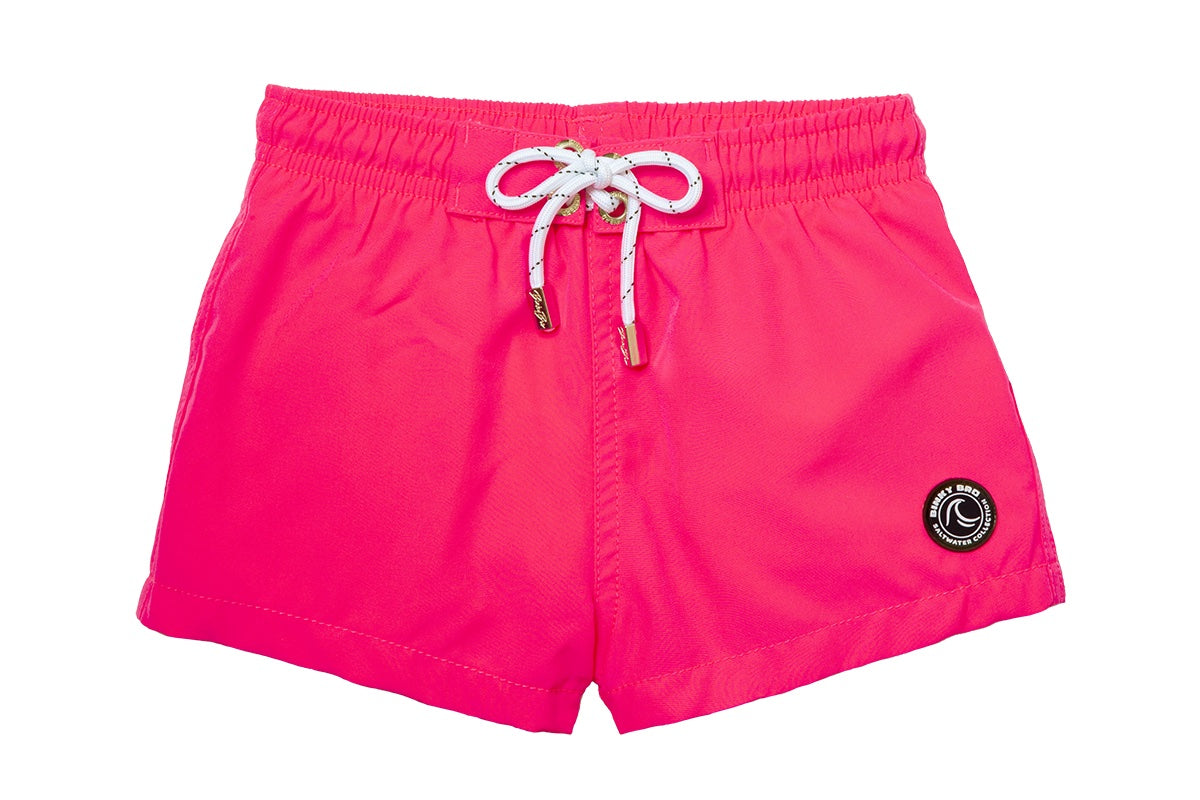 Bright pink swim shorts with an elastic waistband and drawstring, featuring a logo patch on the front. Ideal for kids' summer fun.
