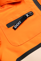 Close-up of the 99-90 BNKY Dragonfire jacket featuring an orange fabric with a zippered pocket and branded tag.