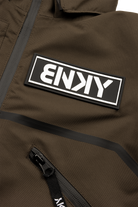 Close-up of a brown jacket featuring a prominent black and white BNKY logo patch and a zippered pocket.