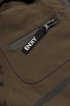 Close-up of a chocolate brown fabric featuring a zippered pocket with a black tag labeled "BNKY," showcasing stylish outdoor apparel.