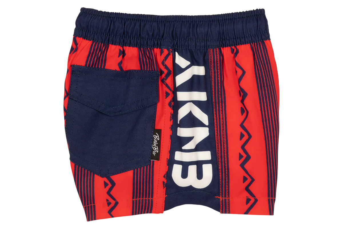 Stylish crimson swim shorts featuring a bold tribal pattern and a navy pocket, perfect for active kids.